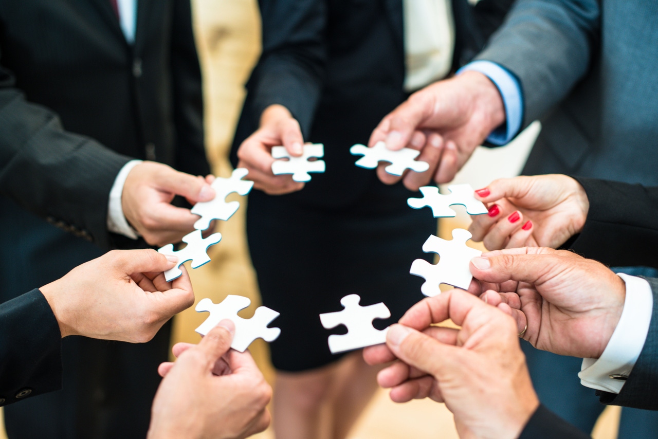 A circle of hands each holding an unconnected puzzle piece.